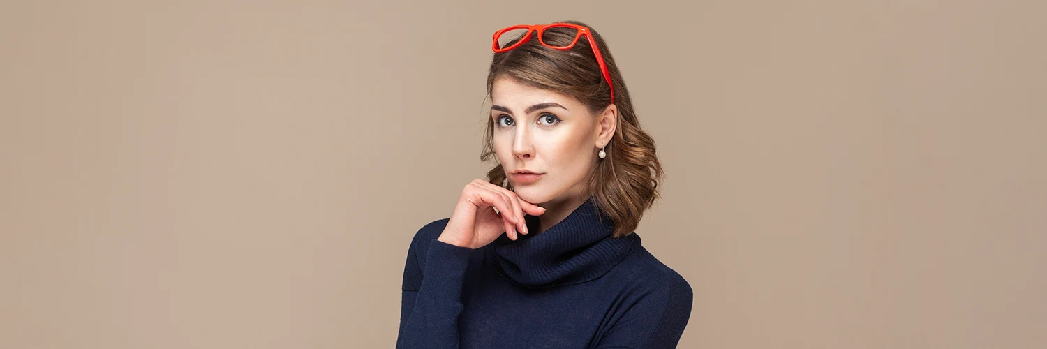 Nachdenkliche junge Frau mit roter Brille auf dem Kopf vor neutralem Hintergrund.