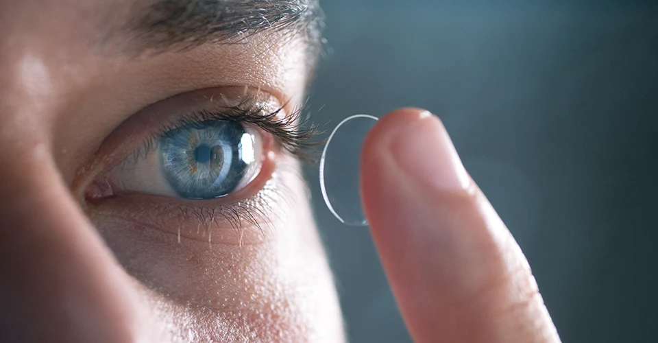 Kontaktlinse wird vor einem geöffneten Auge auf der Fingerspitze gehalten.