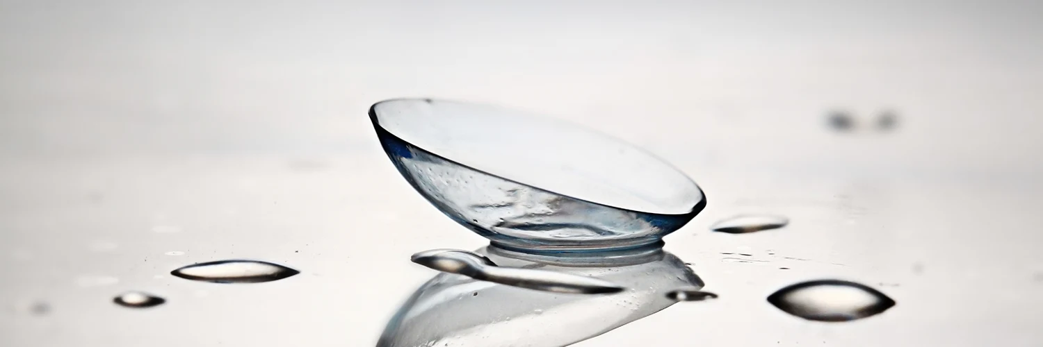 Kontaktlinse liegt zwischen Wassertropfen auf einer glatten Oberfläche.