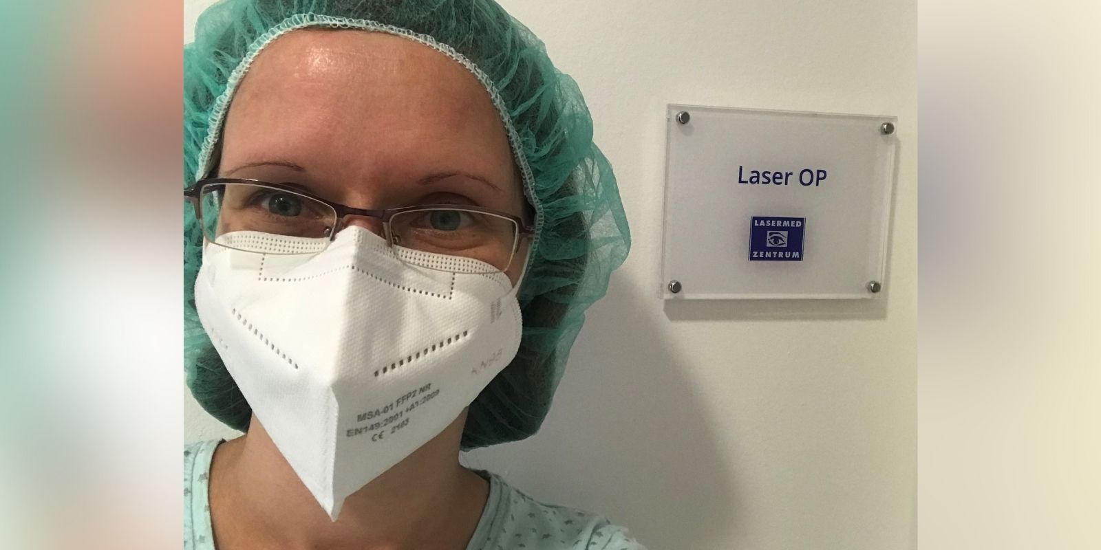 Femto-Lasik Augenlaserbehandlung: Frau mit Brille und OP-Maske vor dem Laser-Behandlungsraum im Augenlaser-Zentrum in der Schönhauser Allee