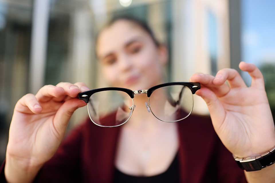 Kurzsichtigkeit: Junge Frau hält Brille weg und sieht in der Ferne unscharf