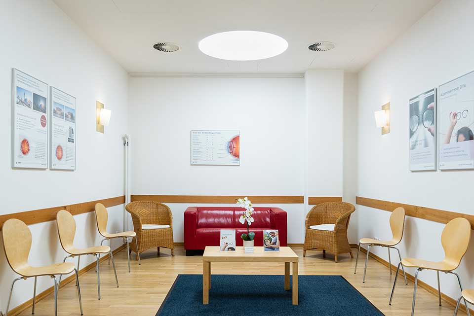 moderner offener Wartebereich mit Holzstühlen und roter Couch im Augenlaser-Zentrum in den Spandau Arcaden von Lasermed